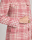 Model wearing The Lady Check Wool Coat in pink—a single-breasted, tailored coat featuring a pink and cream check pattern, functional flap pockets, and fabric-covered buttons, exuding practical femininity and quintessential elegance. Close up of sleeve and button detail.