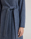 Model wearing the Louise Herringbone Funnel Wool Coat in blue—a sophisticated outerwear piece featuring classic tailoring with a contemporary twist. Detail view of tied belt.