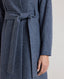 Model wearing the Louise Herringbone Funnel Wool Coat in blue—a sophisticated outerwear piece featuring classic tailoring with a contemporary twist. Detail view of tied belt.