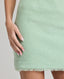 A model wearing the Gabrielle Wool Bouclé Skirt in Green, made from 100% British wool. This textured skirt features a refined silhouette and a signature bouclé weave, with classic green tones that add a touch of modern sophistication. Front view detailed view.