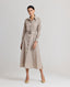 A model wearing the Diane Wool Shirt Dress in Taupe, a mid-length utility dress crafted from 100% pure new wool. This elegant yet practical piece offers a luxurious blend of comfort and style, making it perfect for transitioning from day to night. Front view.