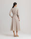 A model wearing the Diane Wool Shirt Dress in Taupe, a mid-length utility dress crafted from 100% pure new wool. This elegant yet practical piece offers a luxurious blend of comfort and style, making it perfect for transitioning from day to night. Back view.