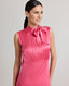 Close-up front view of model wearing Celeste Liberty Silk Dress In Coral, showcasing the high neck and pleat details.