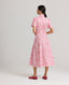 Back view of model wearing the Isabella floral cotton shirt dress made from Liberty fabric. the dress features a short-sleeve button-up design with a collared neckline, a cinched waist with matching fabric belt, and a flowing mid-length skirt. the pink and white floral print adds a delicate, feminine touch.