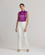 Model wearing the Nicole Liberty Silk Tie Neck Blouse In Amethyst with Meryl slim straight trousers in white. This Nicole blouse is sleeveless and comes with detachable tie at neck, bound armholes and pleat details at front.