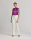 Model wearing the Nicole Liberty Silk Tie Neck Blouse In Amethyst with Meryl slim straight trousers in white. This Nicole blouse is sleeveless and comes with detachable tie at neck, bound armholes and pleat details at front.