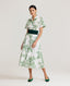 Model wearing the Ella Shirt Dress in Tropical Green. This dress has folded cap sleeves, concealed placket with mother of pearl buttons, hidden pockets at the side seams and comes with a tubular belt in same Tropical Green fabric. Styled with the Forest Green Cummerbund, which is sold separately.