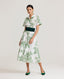 Model wearing the Ella Shirt Dress in Tropical Green. This dress has folded cap sleeves, concealed placket with mother of pearl buttons, hidden pockets at the side seams and comes with a tubular belt in same Tropical Green fabric. Styled with the Forest Green Cummerbund, which is sold separately.