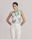 Model wearing the Flora Tie Neck Blouse In Tropical Green. This halterneck  tie blouse has light gathering, covered button fastening at the back and side splits.