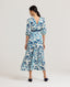 Back view of model wearing our Ivy Tea Dress in a fine blend of silk and cotton, featuring puff sleeve detail and under bust shirring. With delicate floral patterns, this is classic, timeless and feminine. Worn with a navy suede cummerbund.