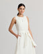 Model wearing the Meryl Fitted Skater Dress In White. This dress features a full skirt and a 5cm wide belt, stab stitching detail, mother of pearl button and rouleaux loop fastening with invisible zip.