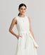 Model wearing the Meryl Fitted Skater Dress In White. This dress features a full skirt and a 5cm wide belt, stab stitching detail, mother of pearl button and rouleaux loop fastening with invisible zip.