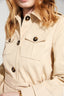 Close-up of a beige trench coat with black buttons on a neutral background