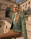 Woman in a green boucle jacket sitting on steps in front of a stone building