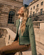 Woman in a green boucle jacket sitting on stone steps with classical architecture in the background