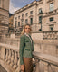 Woman in a green boucle jacket standing on a stone balcony with a classical building in the background