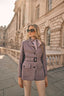 Woman in a purple safari jacket standing in front of an architectural building.