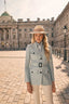 Woman in a blue safari jacket and beige fedora standing in front of a historic building.
