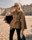 Woman in a beige trench cape standing on a paved square with classical architecture in the background