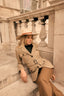 Woman in a beige safari coat and hat sitting on stone steps.