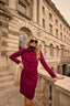 Woman in a purple blazer and skirt standing on a stone balcony with a classical building in the background