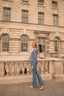 Woman in a blue suit standing on a stone balcony with classical architecture in the background