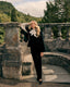 A model wearing A black velvet cape with notched lapels, three front buttons, and a peplum waist.