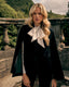 A model wearing A black velvet cape with notched lapels, three front buttons, and a peplum waist.