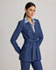 Model wearing the Olivia Wool Linen Tie Belted Jacket in denimâ€”a fitted jacket crafted from a luxurious wool-linen blend, featuring a tie belt and denim-like appearance, perfect for pairing with jeans or elevating evening wear. Side view