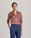 Model wearing the Sidney Paisley Liberty Silk Shirt in fiery orange-red—a 100% silk satin shirt featuring a paisley pattern, designed to elevate both country and city looks. Pair it with tailored trousers for a refined, office-ready ensemble, or dress down with jeans for a relaxed look. Front view.