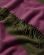 A close-up of a soft woven textile with a diagonal color-block pattern in magenta pink and olive green, finished with fringed trim.