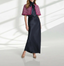 Woman wearing black silk skirt with silk blouse with a pink boucle capelet in a naturally lit studio