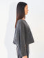A woman shown in side profile wearing a dark gray knit cropped sweater with long sleeves and a crew neckline, paired with dark gray pants, against a plain white background.