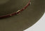 Close-up of a wide-brimmed olive green felt hat with a brown leather band and brass buckle.