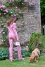 Sophie Stanbury in a pink suit standing in a garden with a dog nearby.