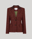 A tailored blazer in a burgundy and brown windowpane check pattern, featuring a dark brown corduroy collar, dark buttons, and flap pockets, displayed against a solid light gray background.