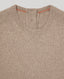 Close-up of a ribbed knit crewneck sweater in a warm taupe-beige color, showing the inner collar with orange contrast stitching.