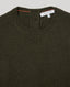 Close-up of a ribbed knit crewneck sweater in dark olive green, showing the inner neck label which reads 'REALITY WILD'.