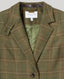 Close-up of a tweed wool-blend jacket in olive green with beige and brown windowpane lines, featuring a white 'REALLY WILD LONDON' neck label.