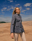 Woman in a boucle jacket standing in a beach landscape with a blue sky.