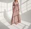 Woman wearing a long pink dress standing in a sunlit room with shadows on the wall.