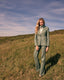 Woman in a green suit standing in a grassy field with a blue sky.