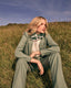 Woman in a green suit sitting in a grassy field with a blue sky.