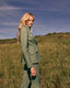 Woman in a green suit standing in a grassy field with a blue sky.