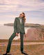 Woman in a green suit standing on a coastal landscape with cliffs and beach.