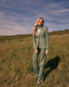Woman in a green suit standing in a grassy field with a blue sky.