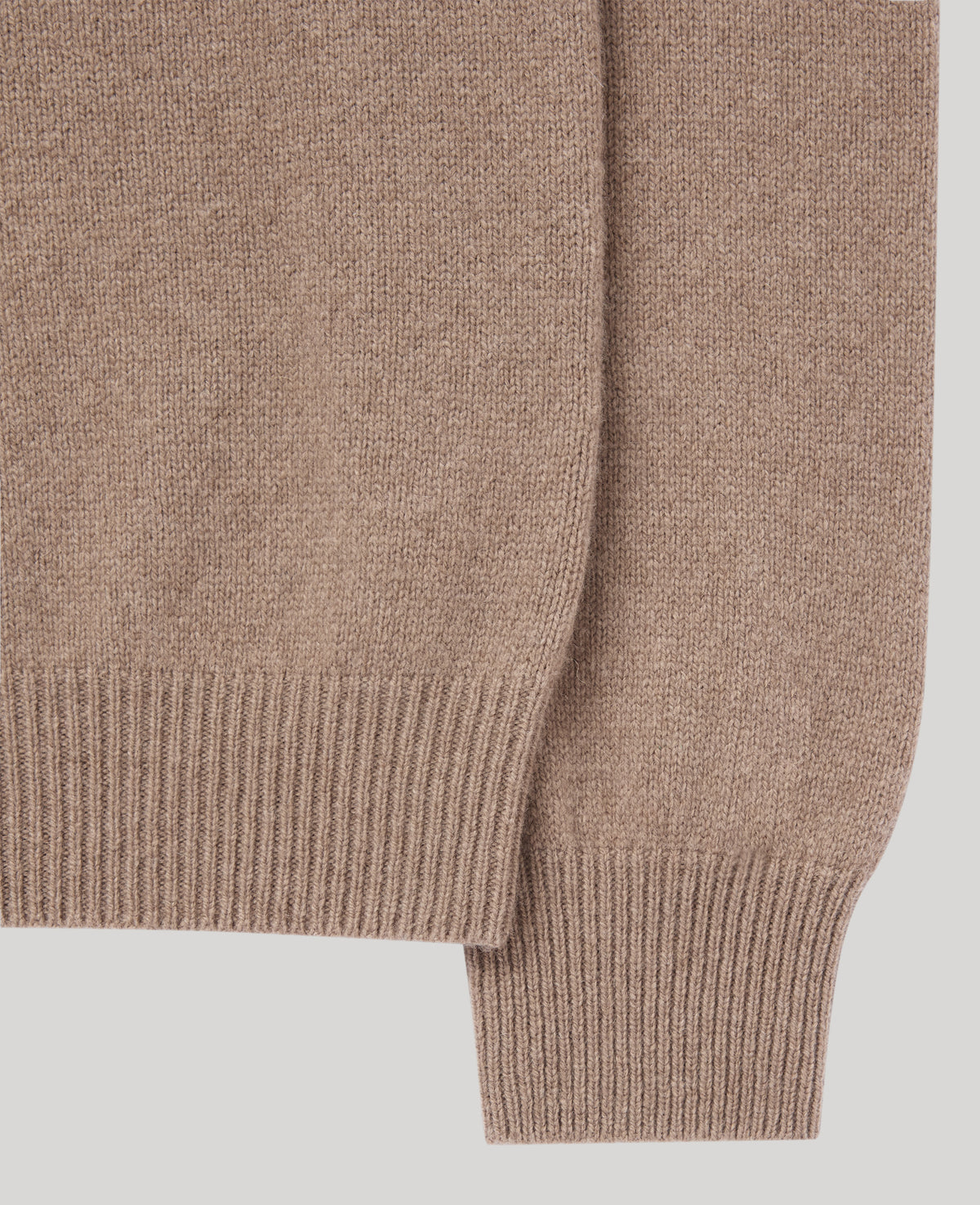 Close-up of a ribbed knit sweater sleeve in a warm taupe-brown color, showing the fine knit texture and ribbed cuff against a light gray background.