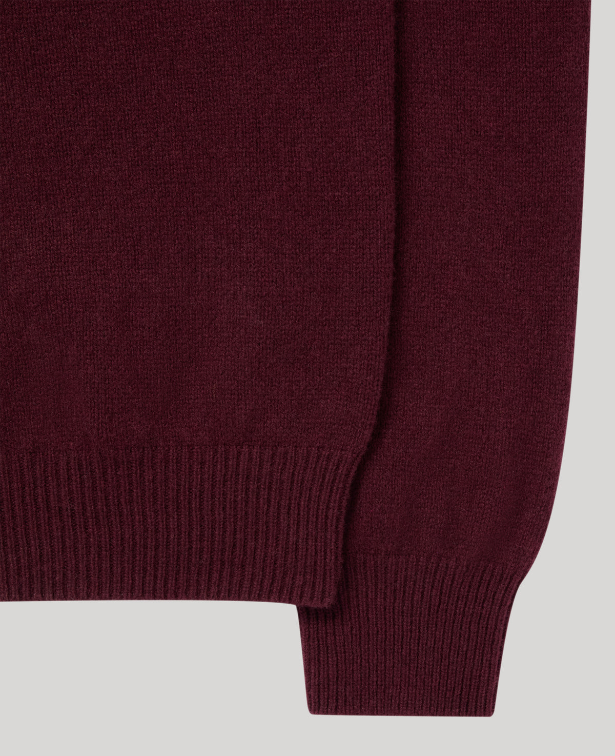 Close-up of a ribbed knit sweater in a deep burgundy or maroon color, showing the texture and cuff detail against a light gray background.