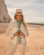 Woman in a white jacket and hat standing on a beach with cliffs in the background