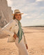 Woman in a white coat and hat standing on a sandy beach with cliffs in the background